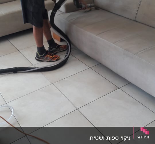 אדם מנקה ספה עם שואב אבק מקצועי